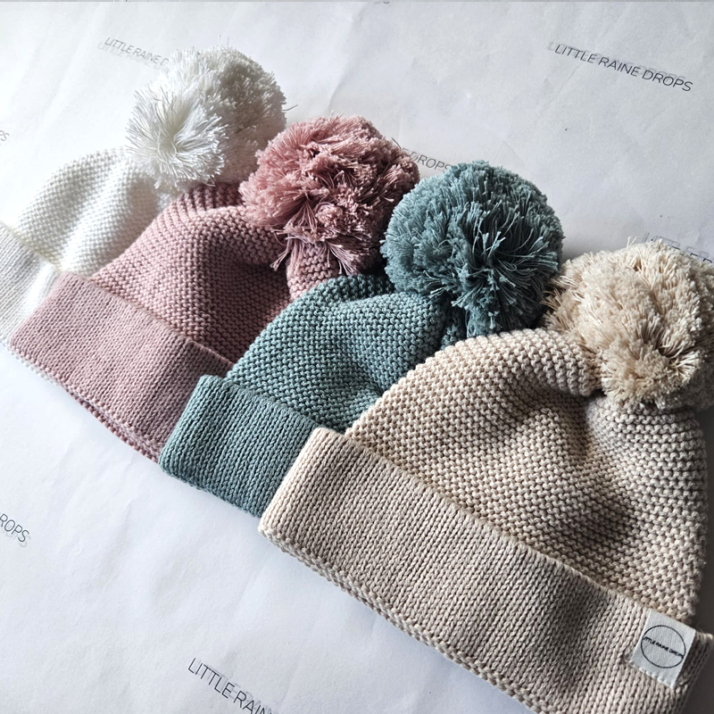 Cotton knit baby hats in pearl, dusky pink, sage and beige with pom pom details, photographed together as a newborn hat collection.