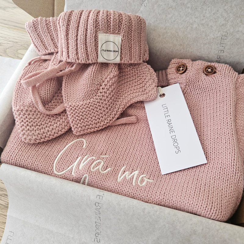 Personalised dusty pink cotton knit baby romper and booties announcement gift set, embroidered with a name and presented in branded gift packaging.