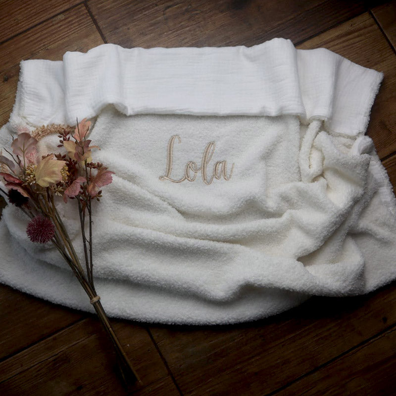 Personalised cosy pearl bouclé baby blanket embroidered with the name Lola, styled with dried flowers for a soft nursery aesthetic.