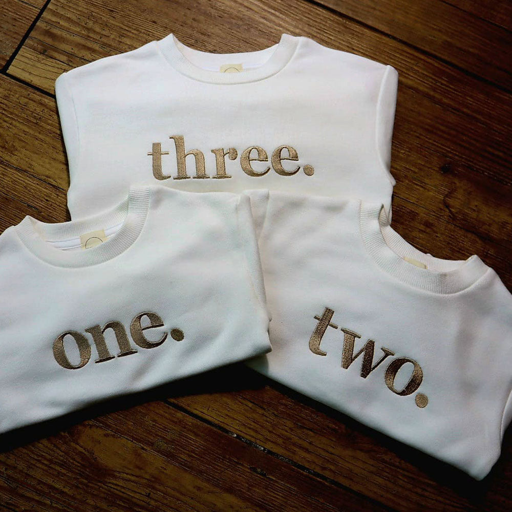Personalised children’s occasion sweatshirts embroidered with “one”, “two” and “three”, stitched by Little Raine Drops.