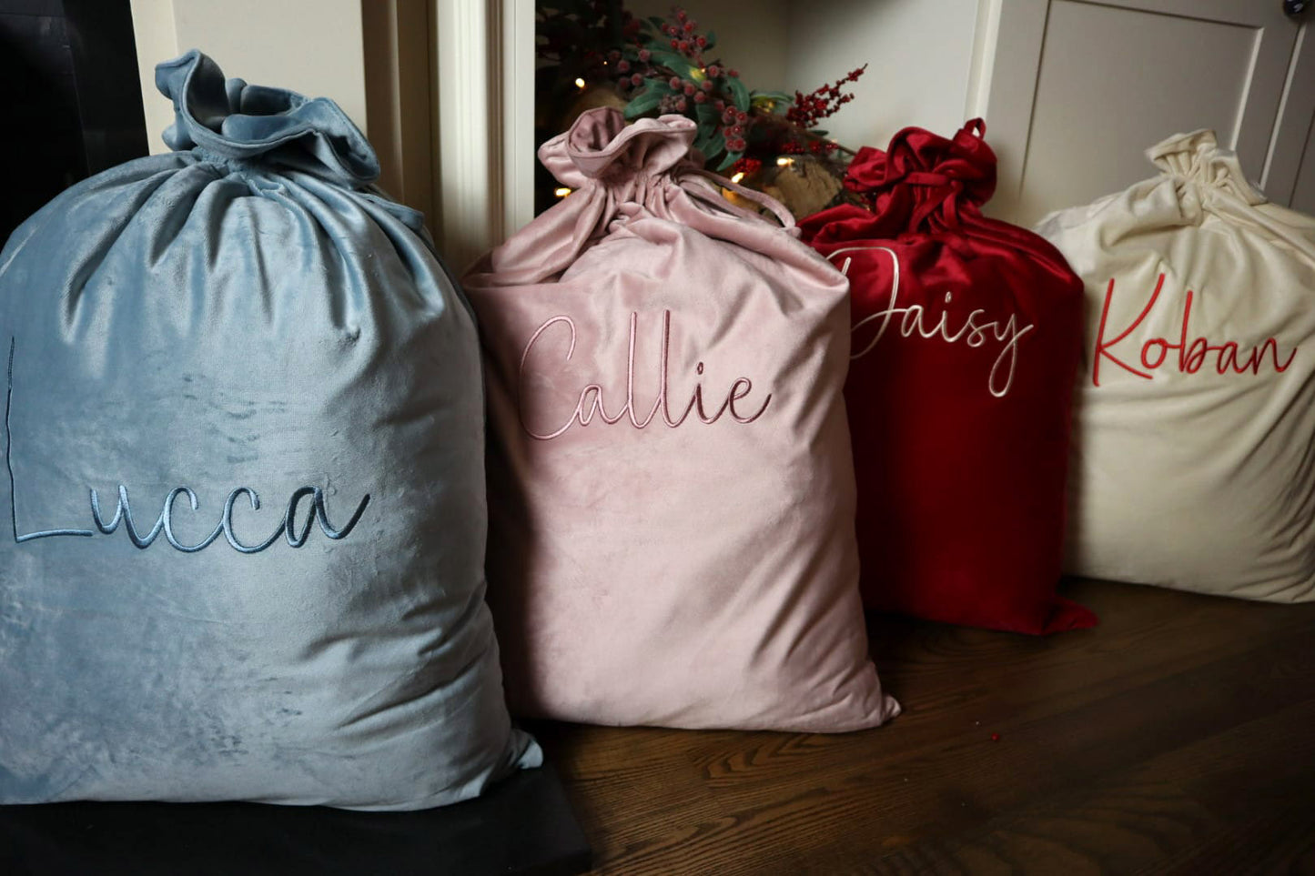 Personalised luxury velvet Santa sacks in dusky blue, dusky pink, rich red and cream, embroidered with children’s names for Christmas gifting.