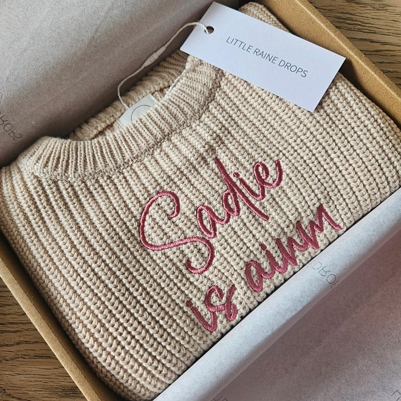 Personalised beige chunky cotton knit baby sweater with embroidered name, styled in Little Raine Drops gift packaging. A timeless newborn and baby shower keepsake