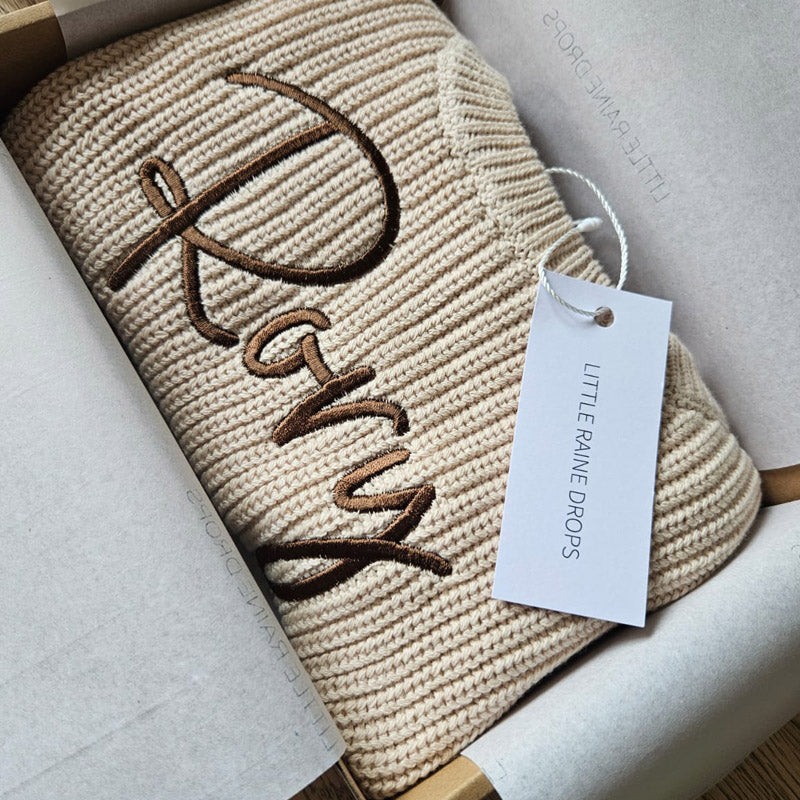 Personalised beige chunky cotton knit baby sweater with embroidered name, styled in Little Raine Drops gift packaging. A timeless newborn and baby shower keepsake