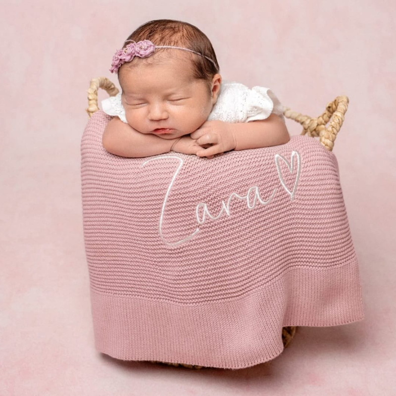 Newborn baby posed in basket with dusky pink personalised cotton knit baby blanket embroidered with name by Little Raine Drops Ireland