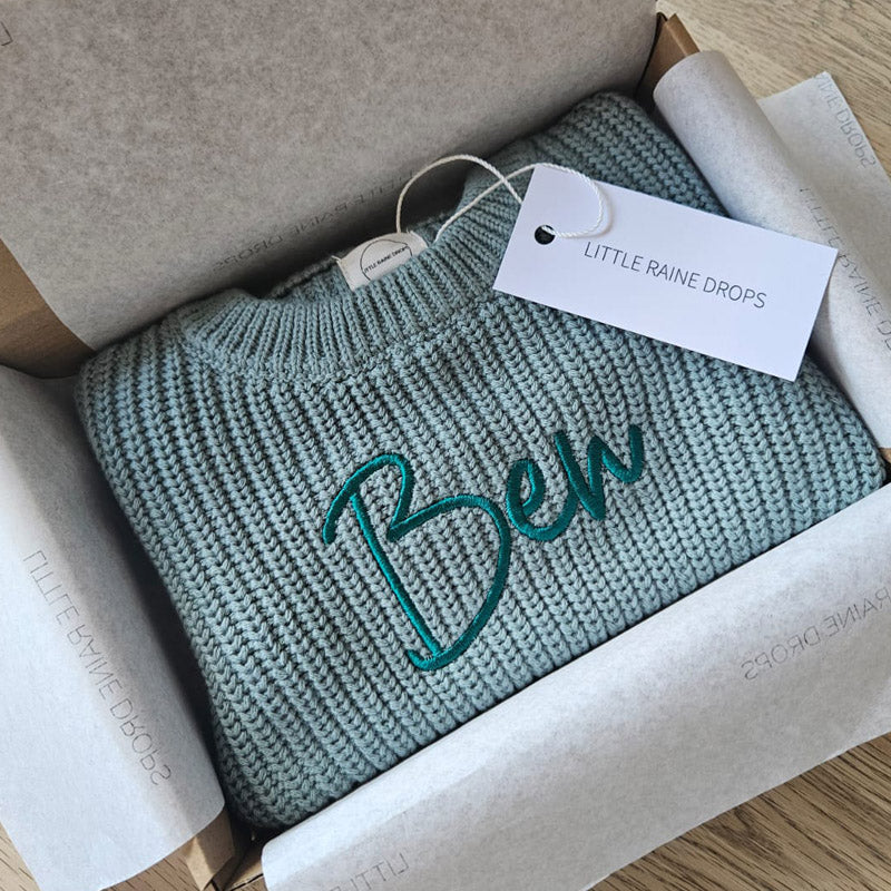 Personalised sage chunky knit baby sweater embroidered with the name “Ben”, neatly folded in branded gift box, luxury baby knitwear by Little Raine Drops.