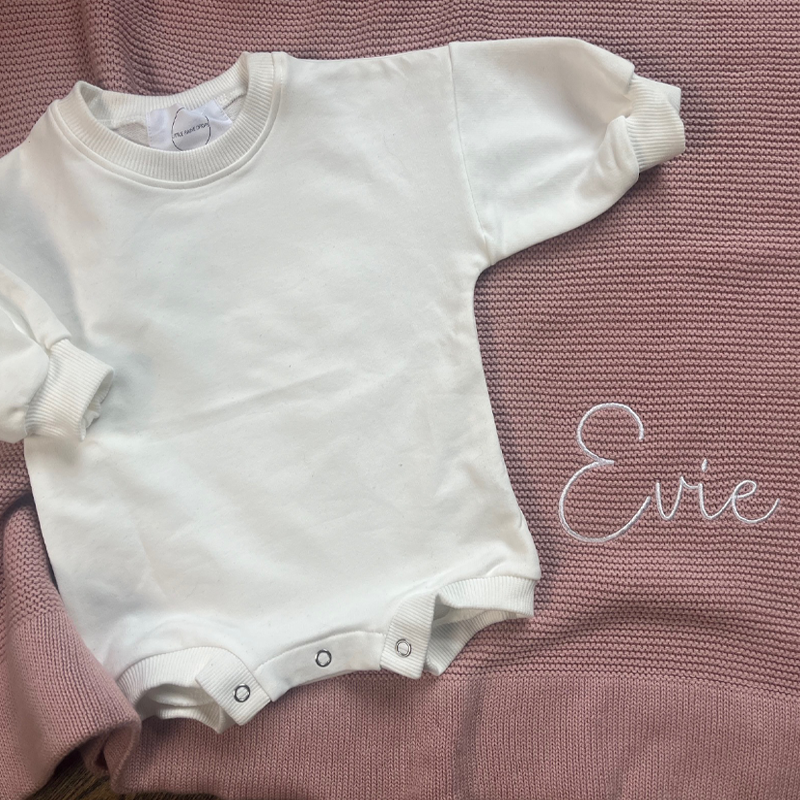 Milk coloured baby bubble romper laid flat on dusky pink knit blanket personalised by Little Raine Drops