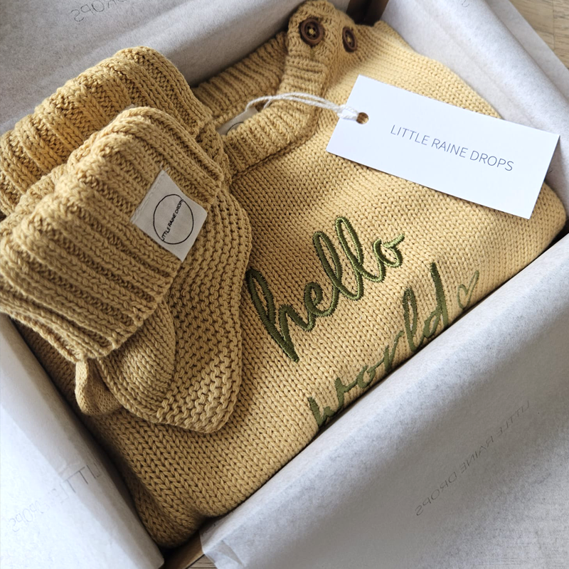 Ochre cotton knit baby romper and matching booties presented in gift packaging with Little Raine Drops tag, personalised newborn announcement made in Ireland.