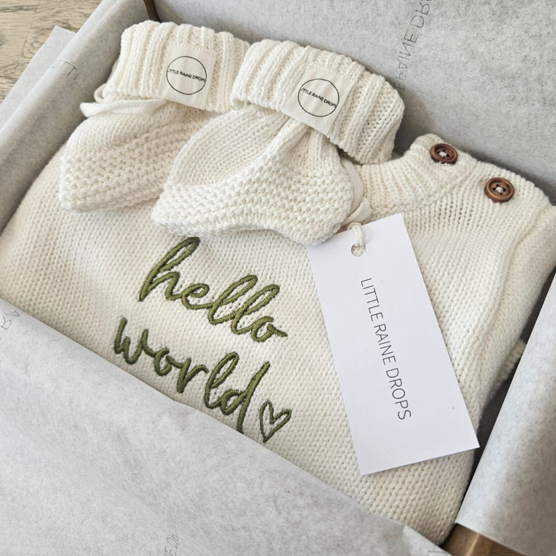 Personalised pearl cotton knit baby romper with matching knit booties, featuring “hello world” embroidery, presented in a Little Raine Drops gift box, a cosy and timeless personalised Announcement set.