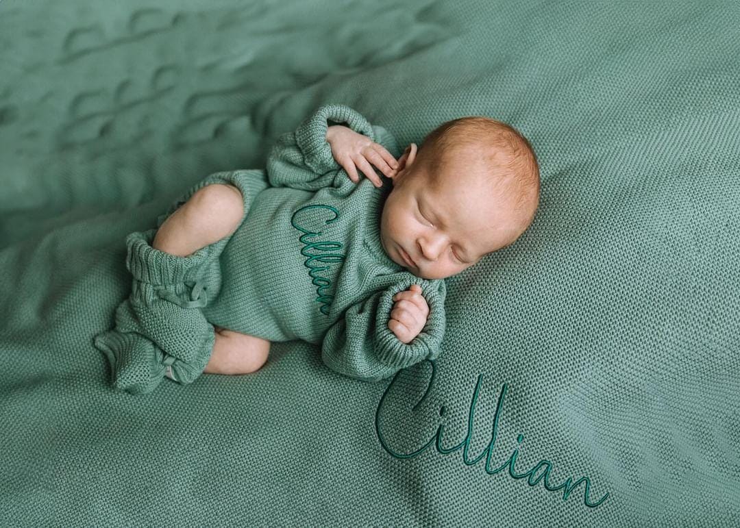 Newborn baby sleeping on a sage cotton knit personalised blanket while wearing a matching sage cotton knit romper and booties, styled for a minimalist baby announcement by Little Raine Drops.