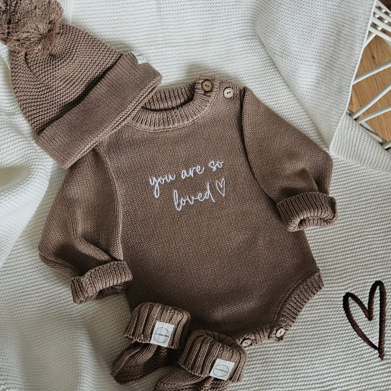 Flat lay of taupe knit baby romper set with matching hat and booties, personalised embroidery by Little Raine Drops.